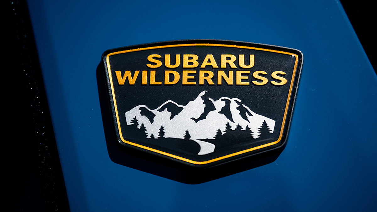 Gold Subaru Wilderness badge with white rocky mountains on exterior of blue Subaru Outback Wilderness SUV.