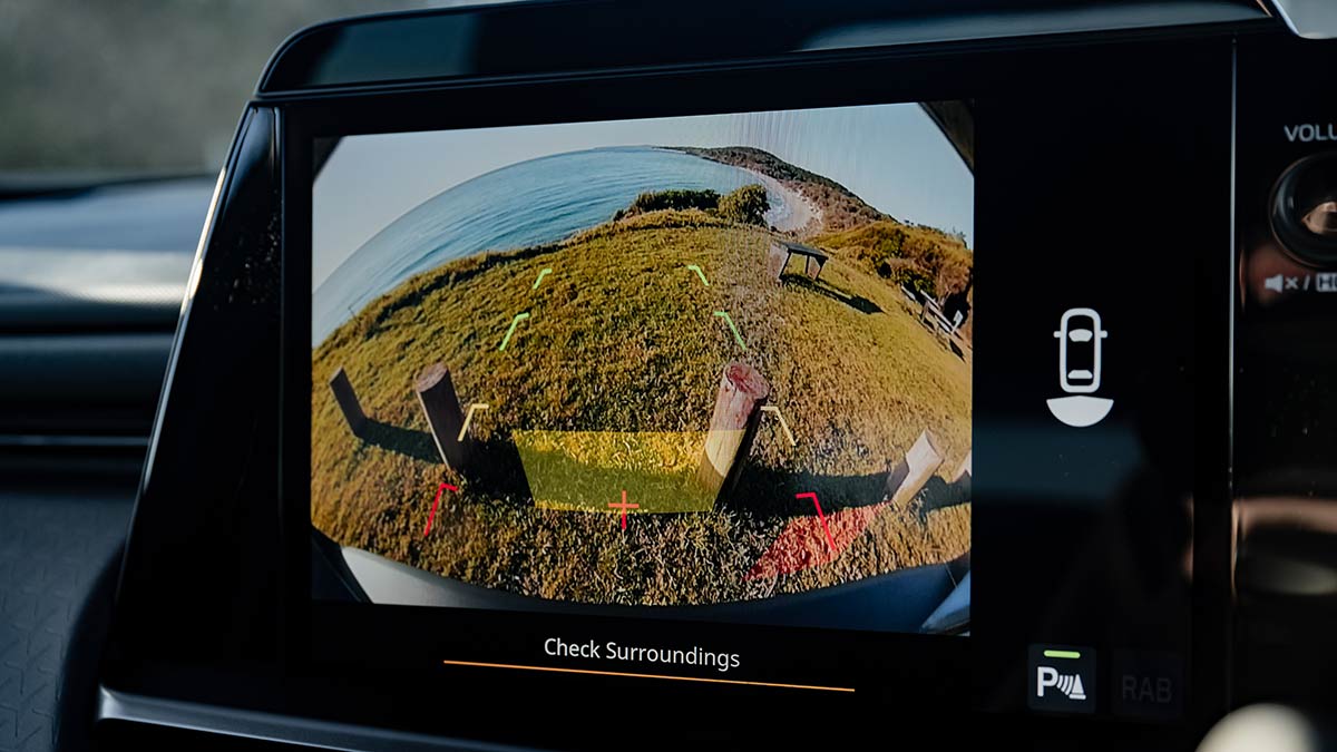 Camera display with guidelines in Subaru Outback Wilderness showing rear view with carpark bollards and ocean.