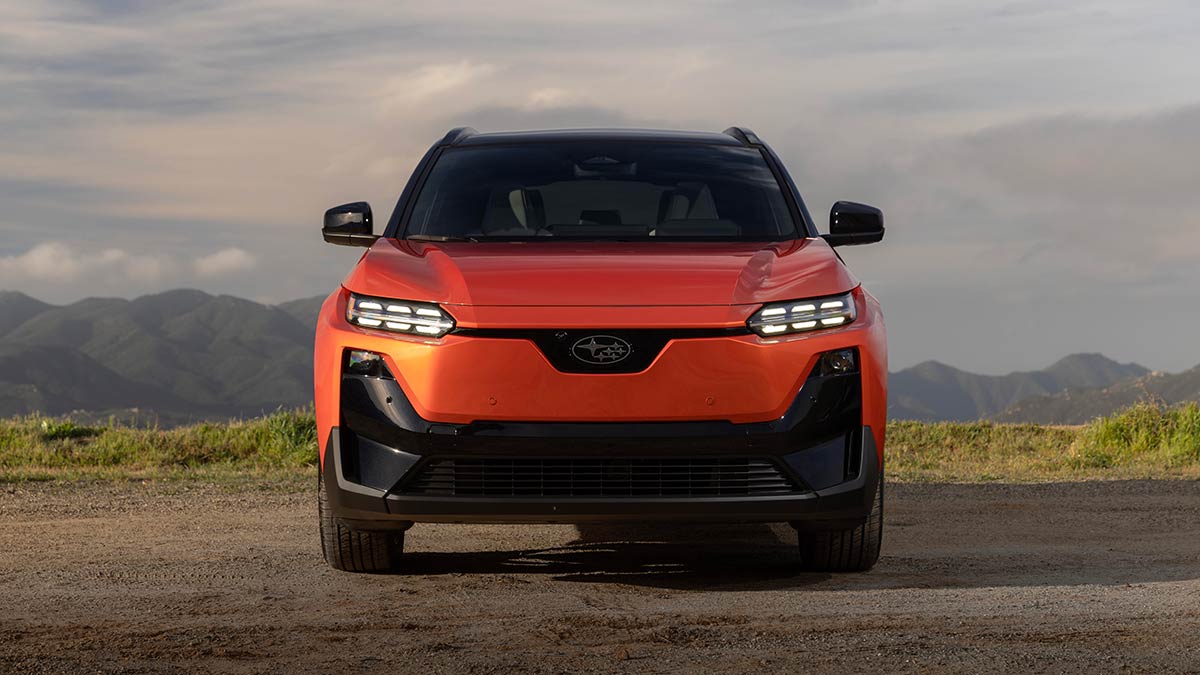 Front-on view of orange metallic Subaru Uncharted small electric SUV parked on gravel at high mountainous location.