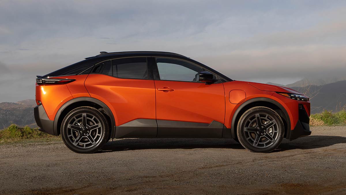 Side-on view of orange metallic Subaru Uncharted small electric SUV parked on gravel at high mountainous location.