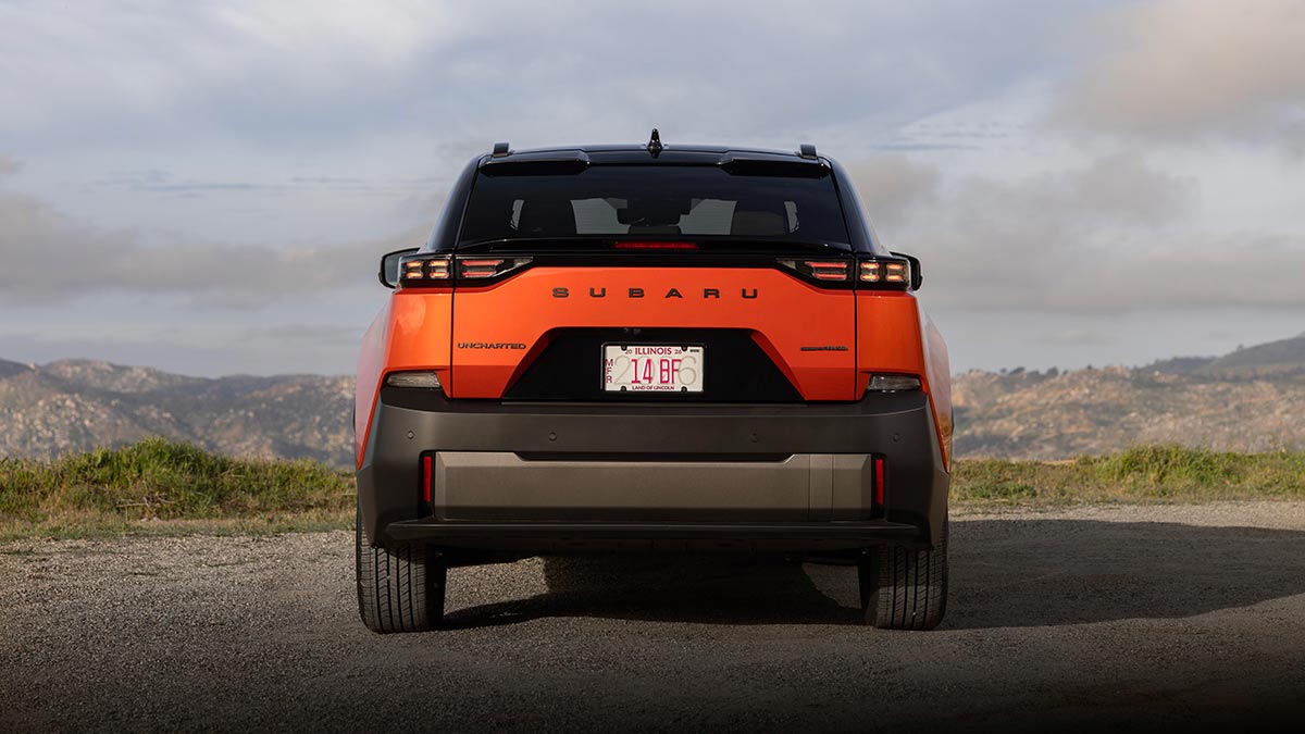 Rear view of orange metallic Subaru Uncharted small electric SUV parked on gravel at high mountainous location.