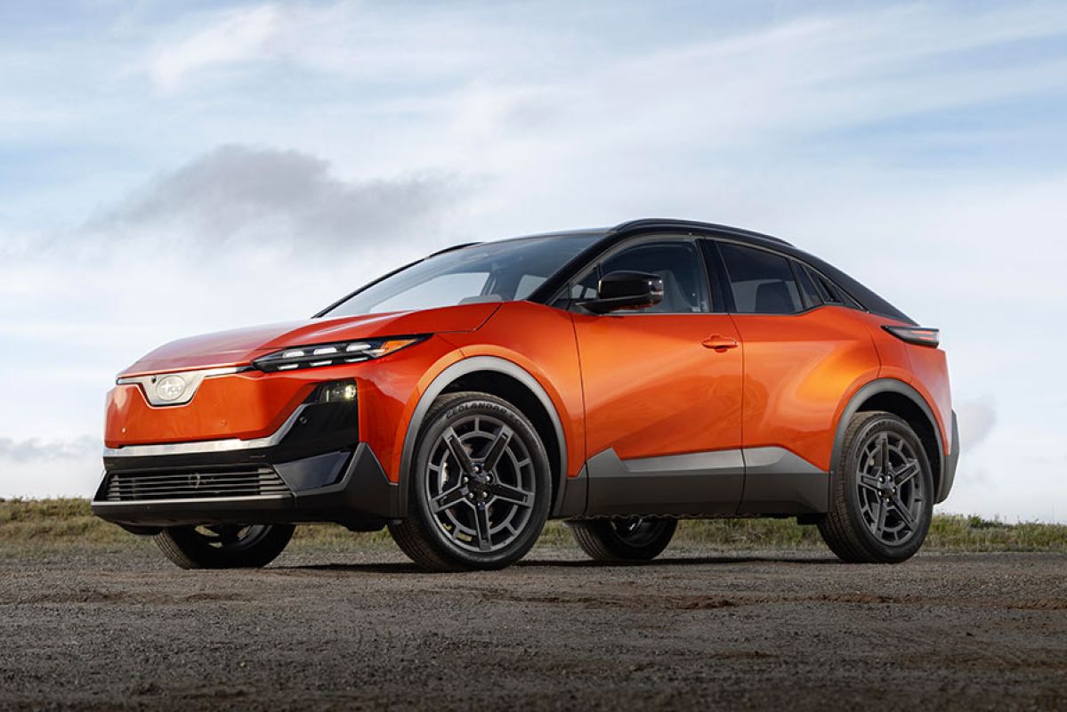 Orange metallic Subaru Uncharted small electric SUV parked on gravel road with skyline in background.