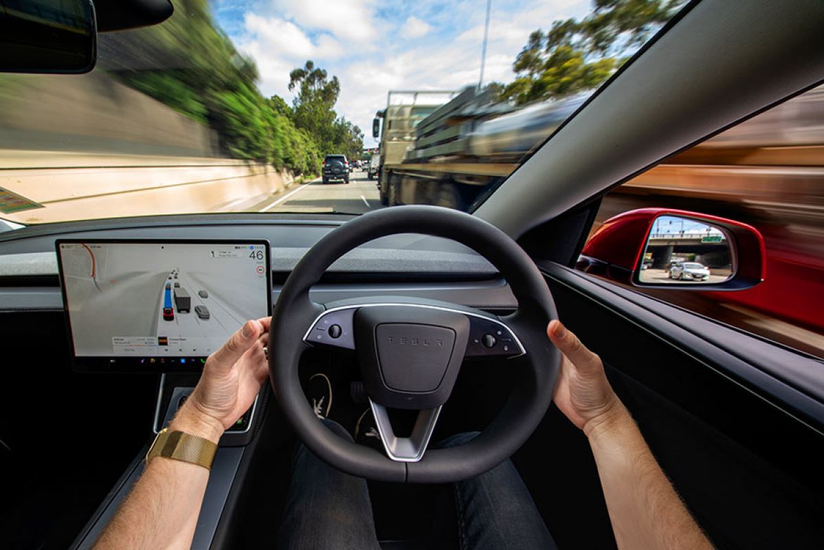Two hands on steering wheel of Tesla Model Y EV while in Full Self Driving (Supervised) mode on busy Victorian multi-lane freeway.