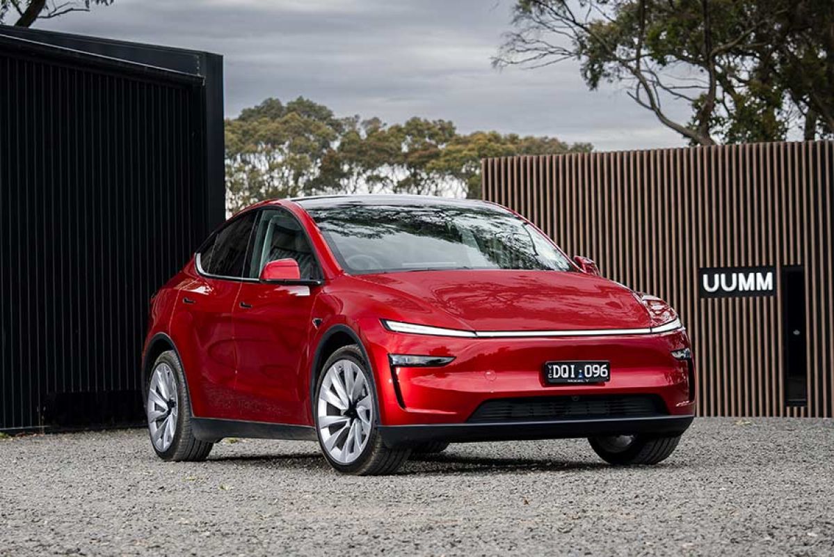 Red Tesla Model Y SUV parked in front of Mt Macedon winery building with black steel door and wooden fence.