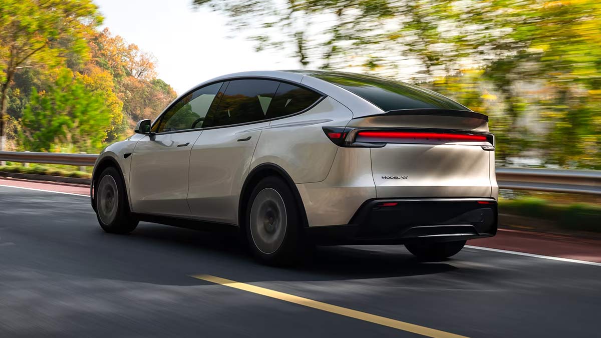 Rear view of light-coloured left-hand-drive Tesla Model Y L SUV on leafy country road.