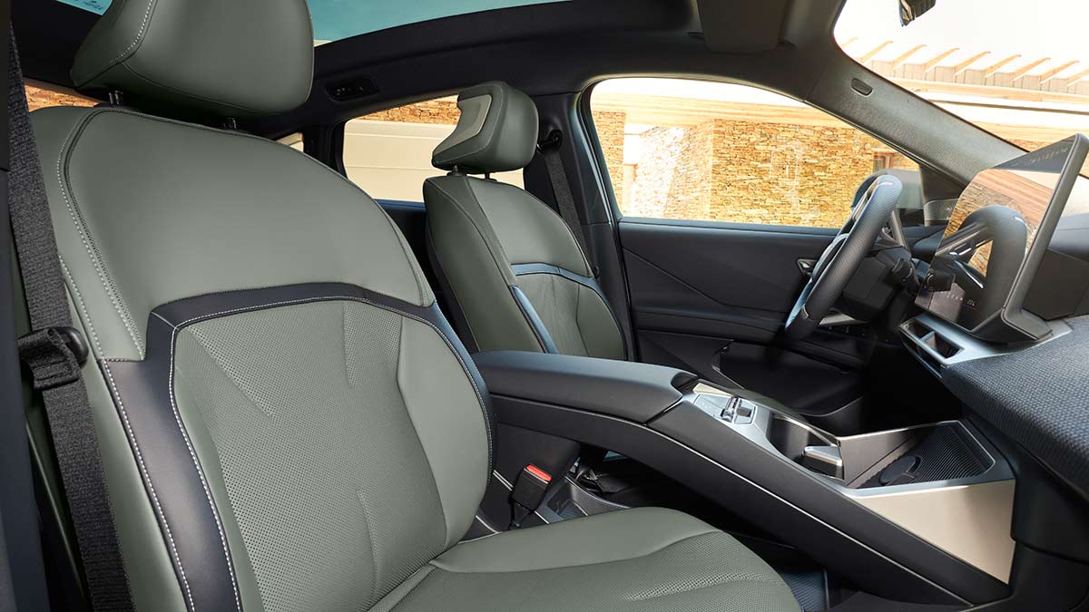 Front seats in BMW iX4 50 xDrive coupe-style SUV as seen from front passenger door, showing agave green upholstery, bridge console, large centre screen.