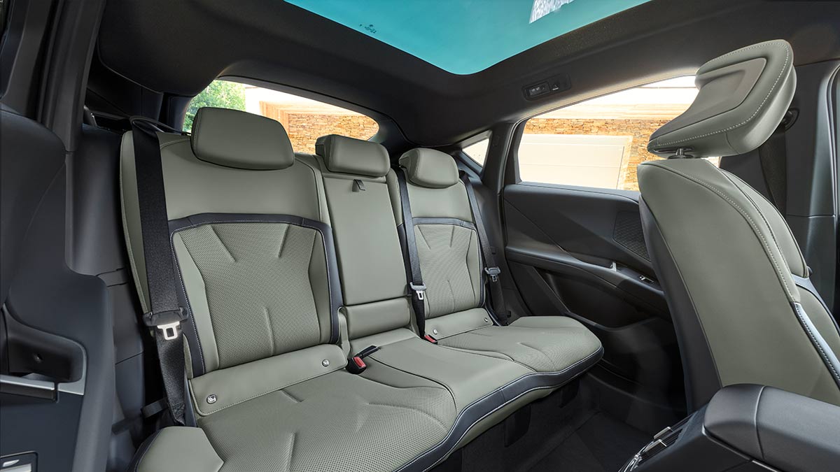 Rear seat area in BMW iX4 50 xDrive coupe-style SUV with sloping roofline, panoramic sunroof and agave green upholstery.