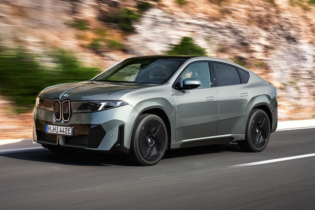 Metallic sage green BMW iX4 50 xDrive coupe-style SUV in left-hand-drive on high-banked coastal road in Europe.