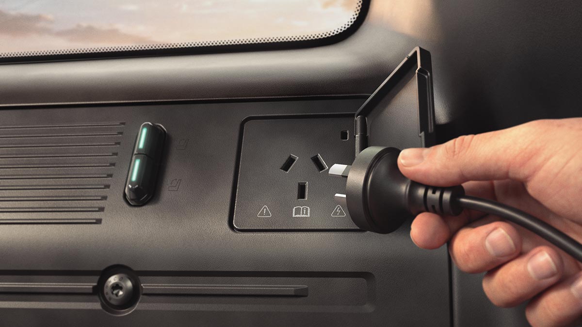 Hand holding power cord close to 3-pin vehicle-to-load outlet in back of Ford Bronco Basecamp SUV.