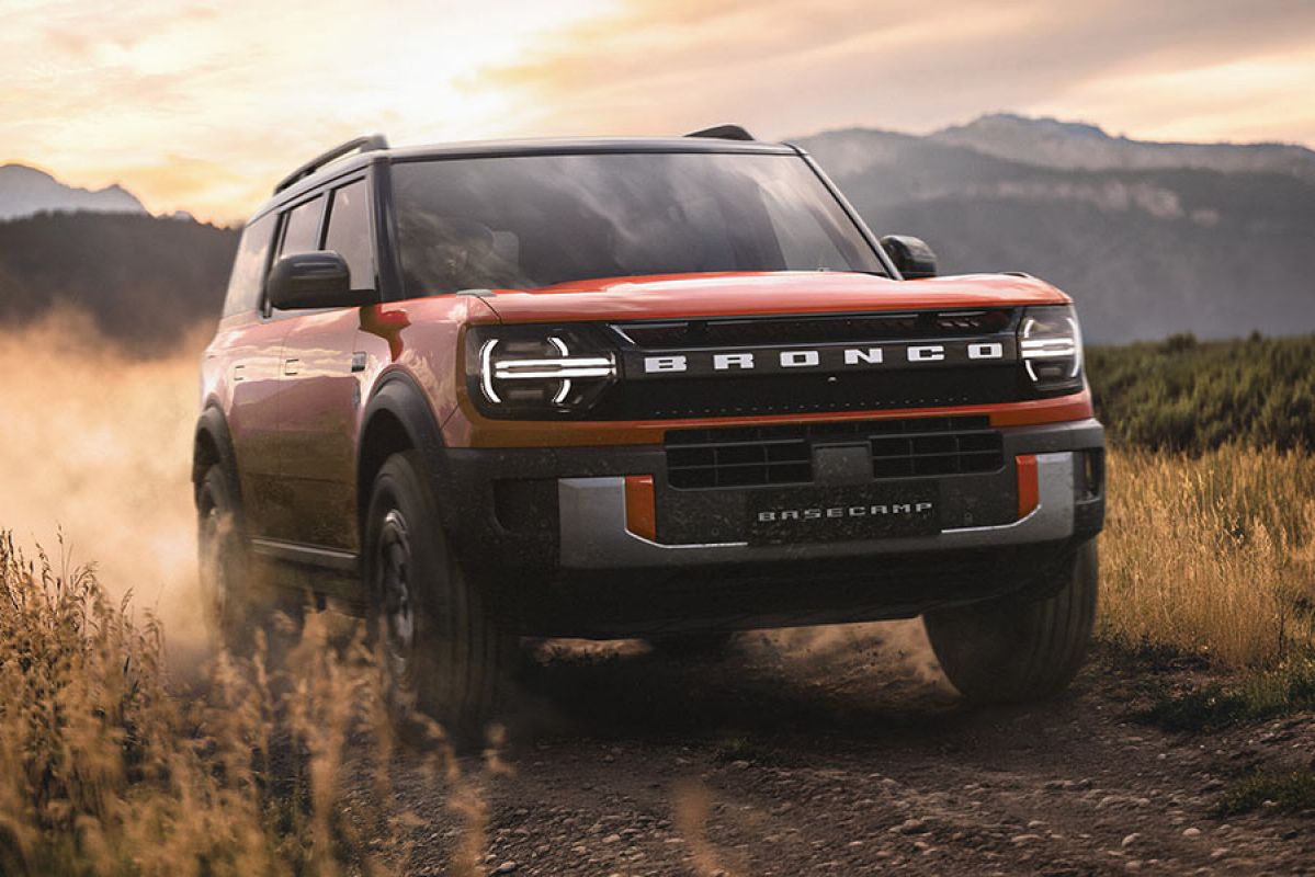 Red Ford Bronco Basecamp plug-in hybrid SUV kicking up dust along narrow grass-lined track in high country.