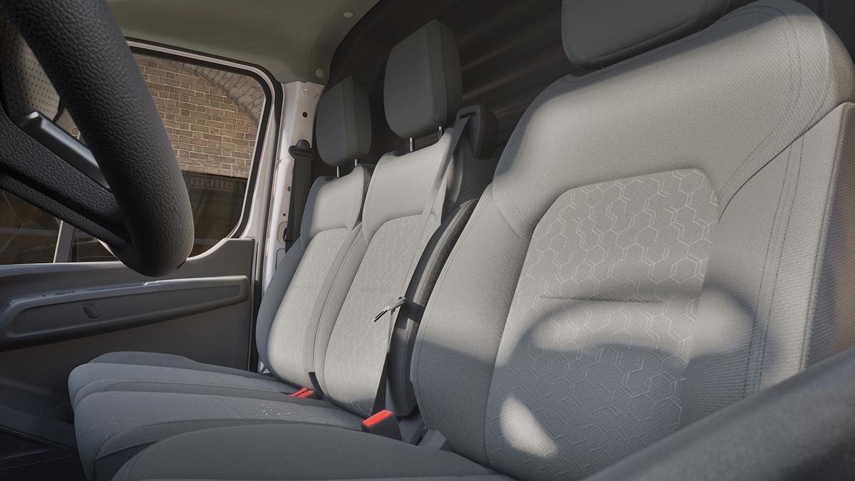 View from front passenger’s door of left-hand-drive Ford Transit City electric van with three seats, cloth trim and storage areas in dashboard.