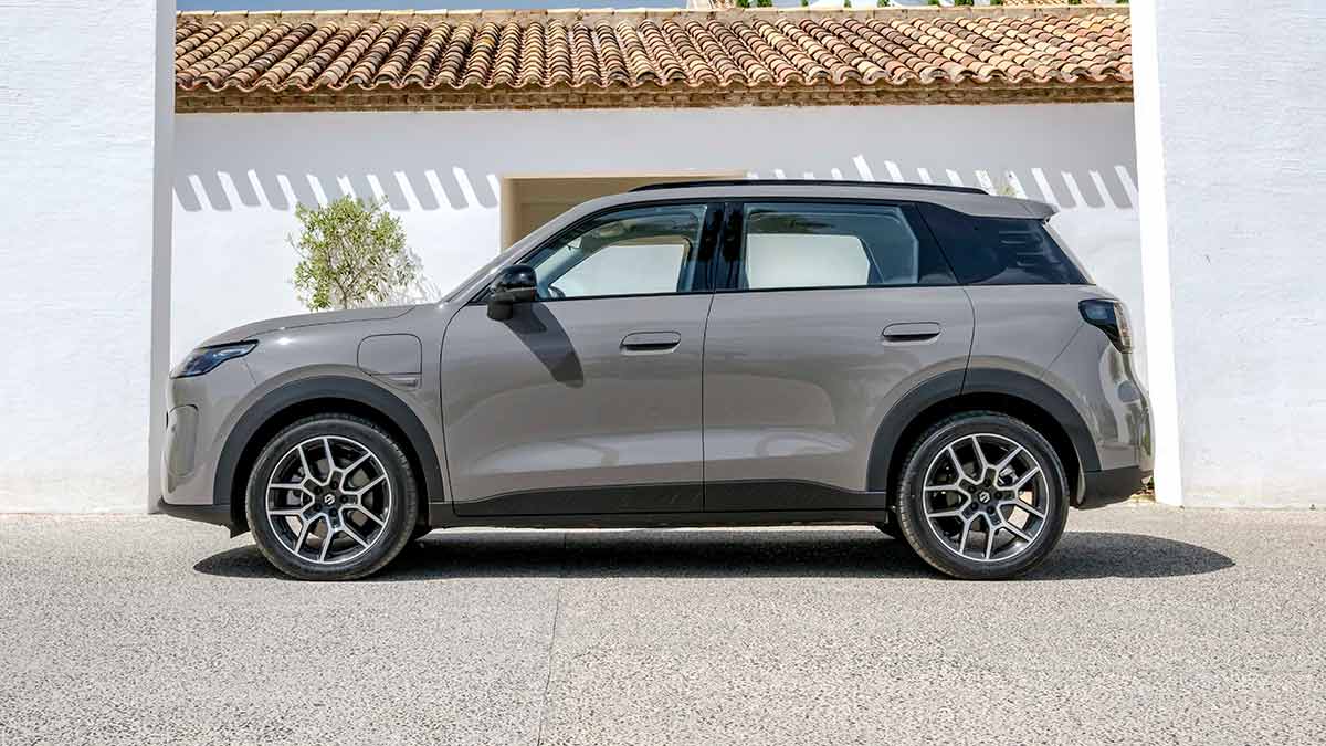 Side profile show of light brown Leapmotor B03X small electric SUV parked outside Tuscan villa with olive tree against white wall.