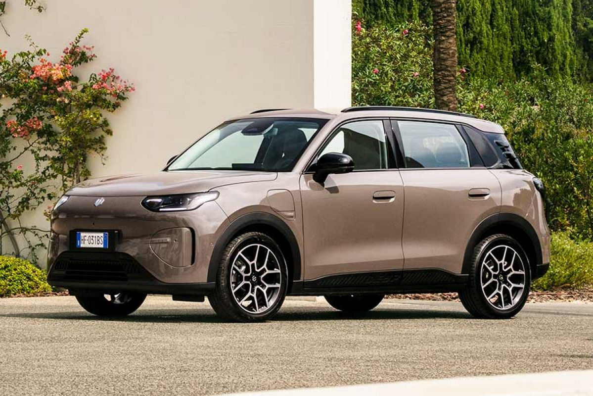 Light brown Leapmotor B03X small electric SUV parked on driveway in outdoor garden setting with thick green shrubbery and white wall with pink rosebush.