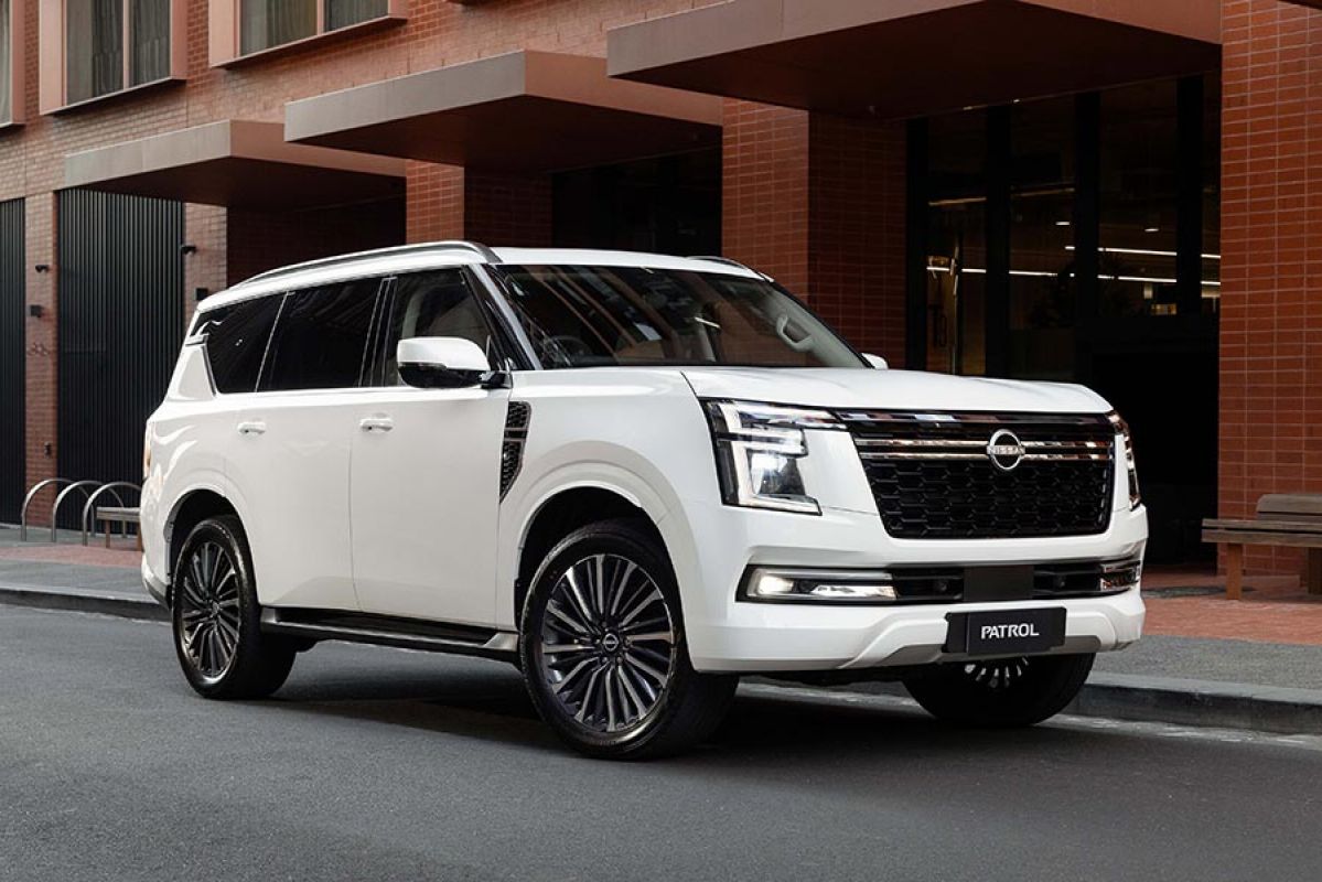 A white Y63 2027 Nissan Patrol SUV parked on a street in front of a red brick industrial office complex.