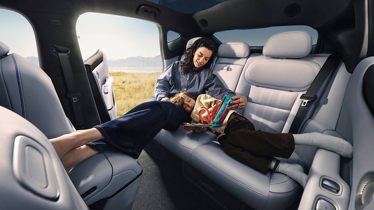 Back seat of XPeng L03 SUV with woman sitting upright and child lying across bench with head in woman’s lap.