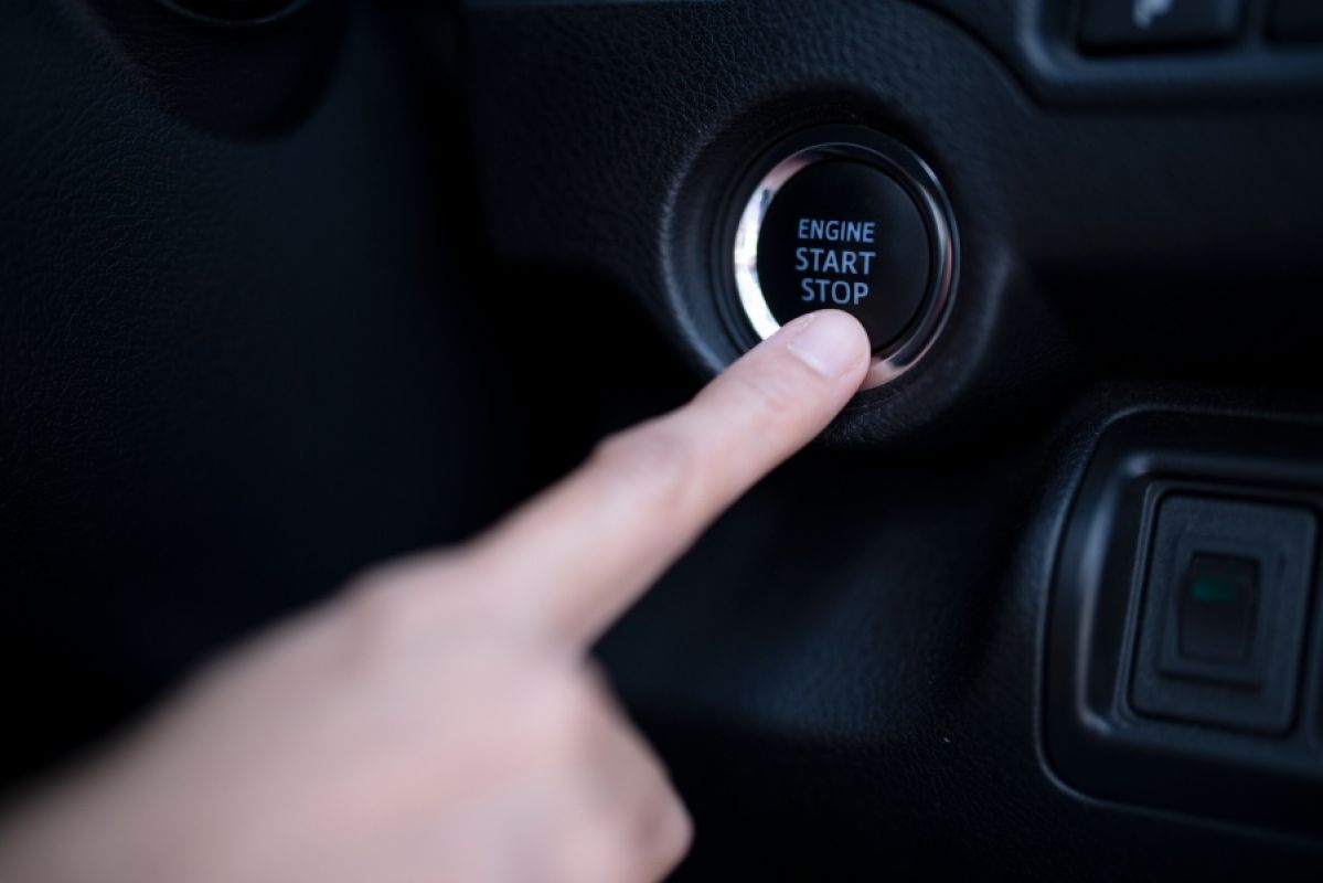 person pushing start button in car