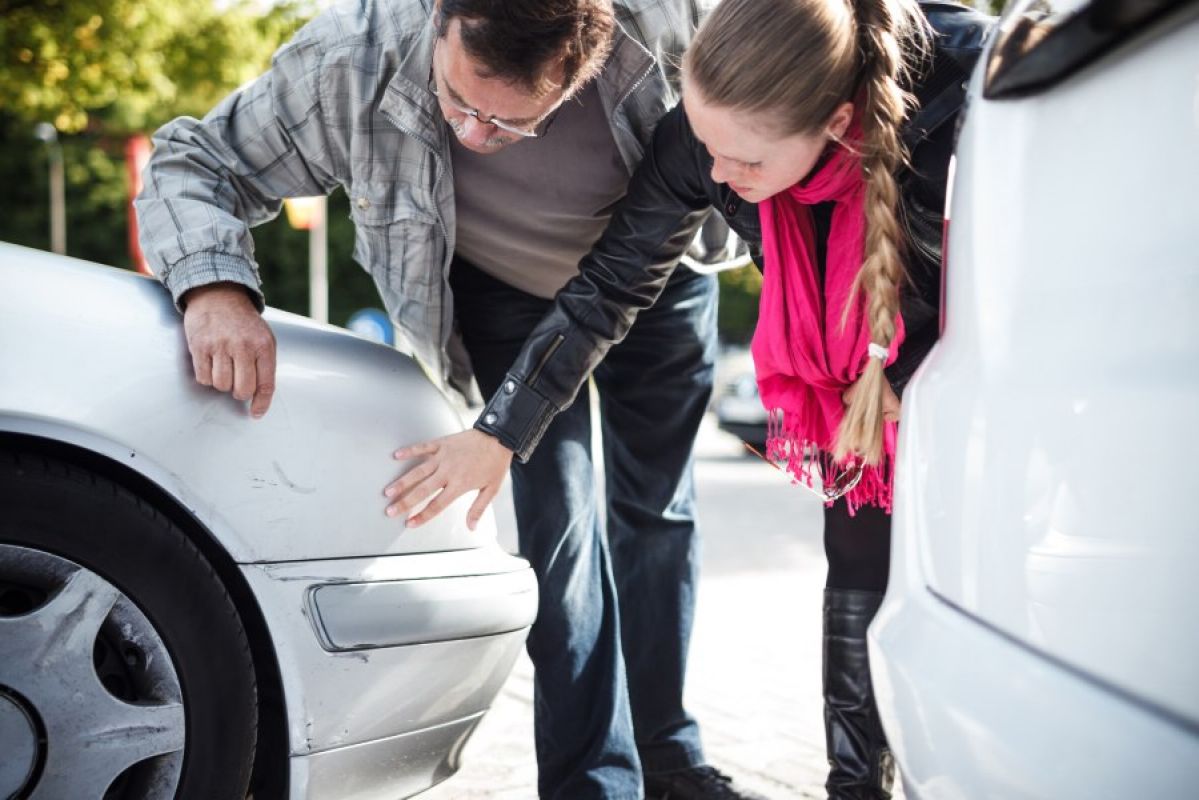 An older man and a younger woman examining a parked car for damage to the bumper