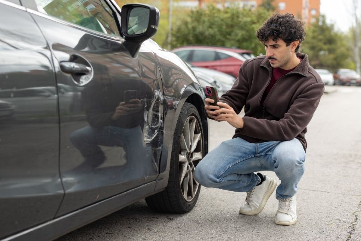 young man taking photo of damage to car after collision