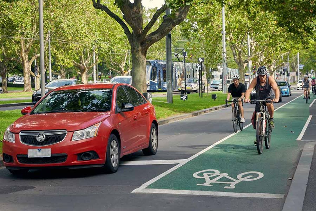 A red car next to a designated bike lane with two bike riders in Melbourne.