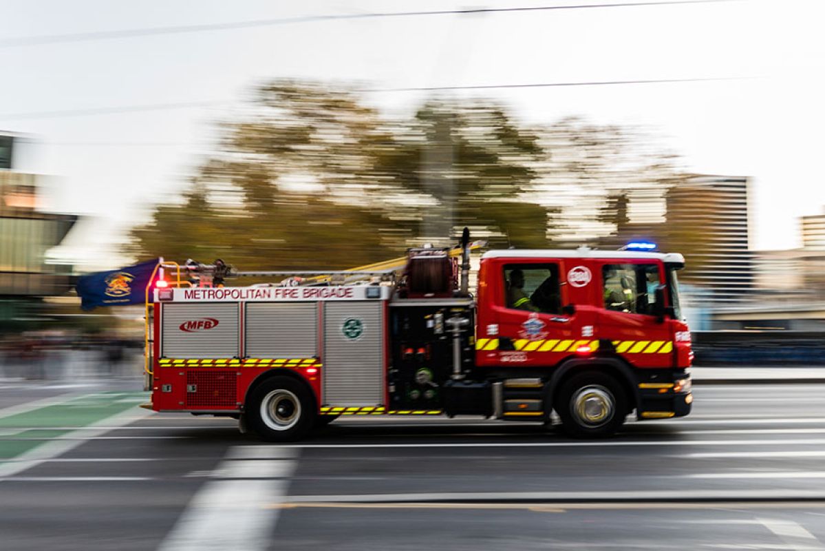 A red fire truck with flashing lights driving along a road in Melbourne