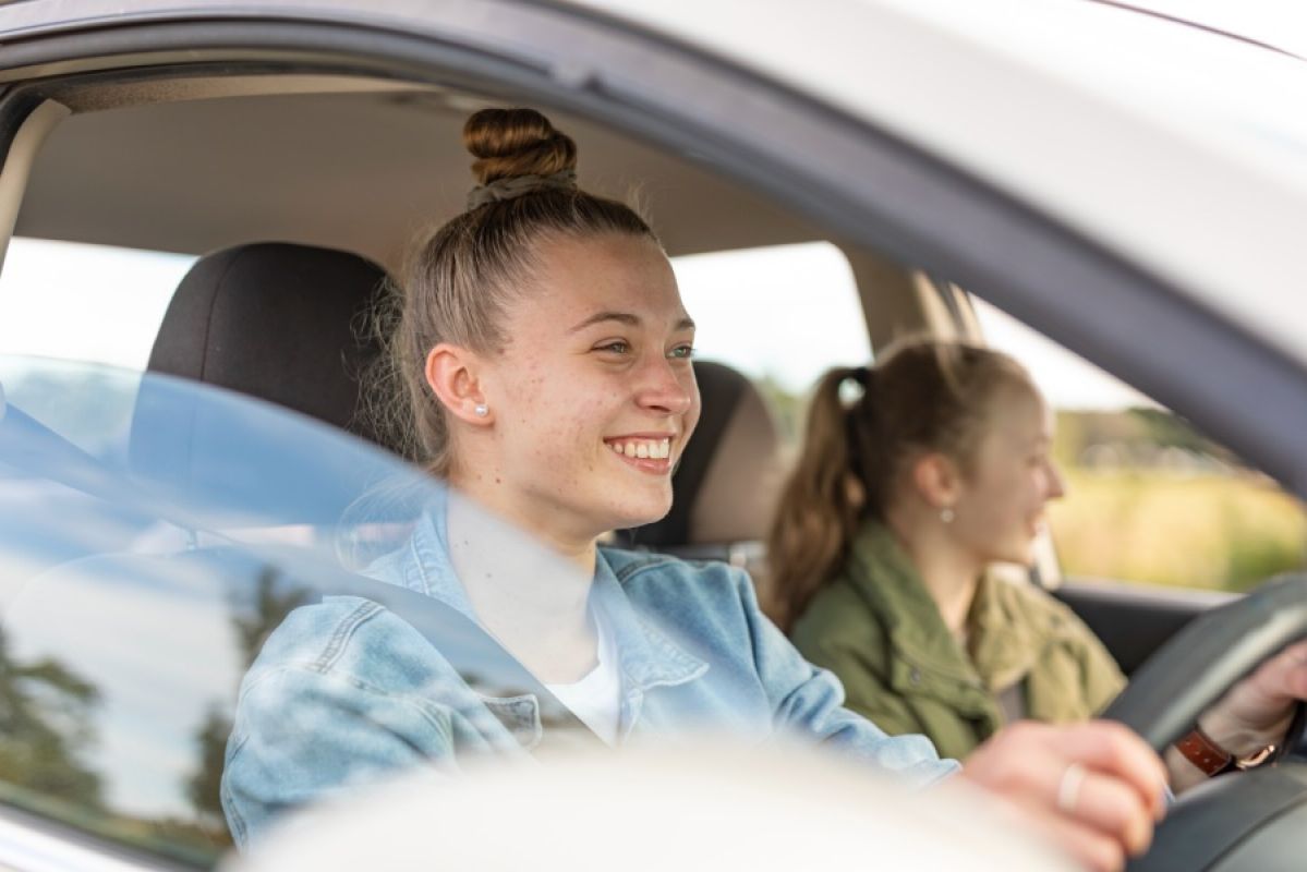 young woman driving a car and smiling with a female passenger