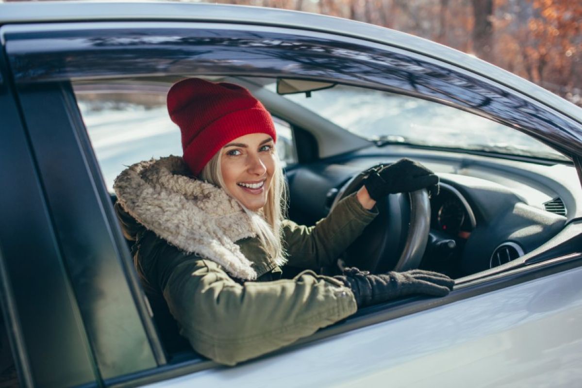 young woman in red beanie and thick winter coat smiling from her parked car
