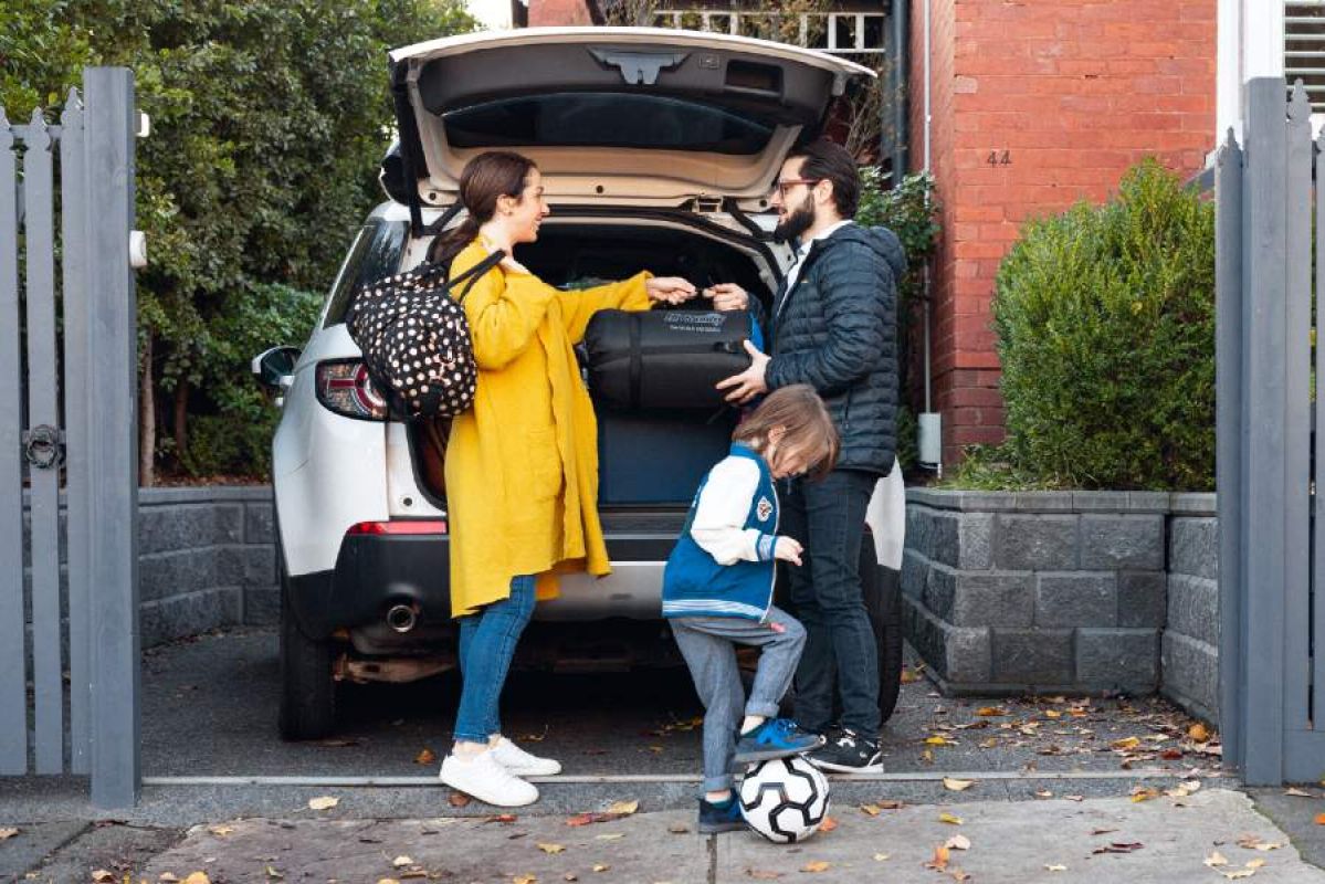 A woman, man and small child with a soccer ball loading bags into a SUV 
