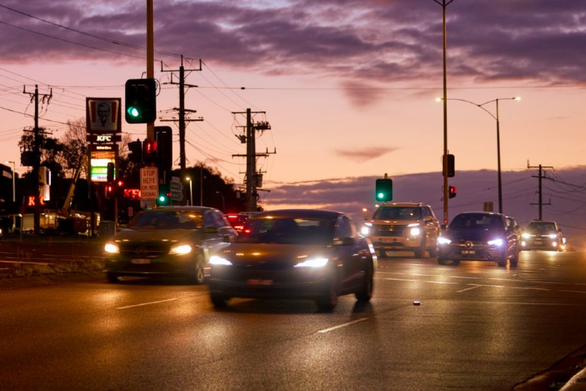 Several cars driving through the intersection of Wantirna and Boronia roads in Wantirna. It is early evening and darkness nearly fallen and the cars have their headlights on