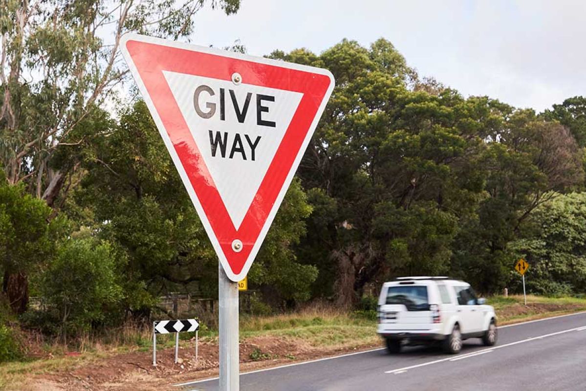 Red and white triangular 'give way' sign with car driving in background