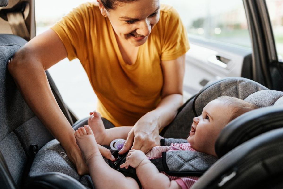 A smiling woman strapping a happy baby into a car seat