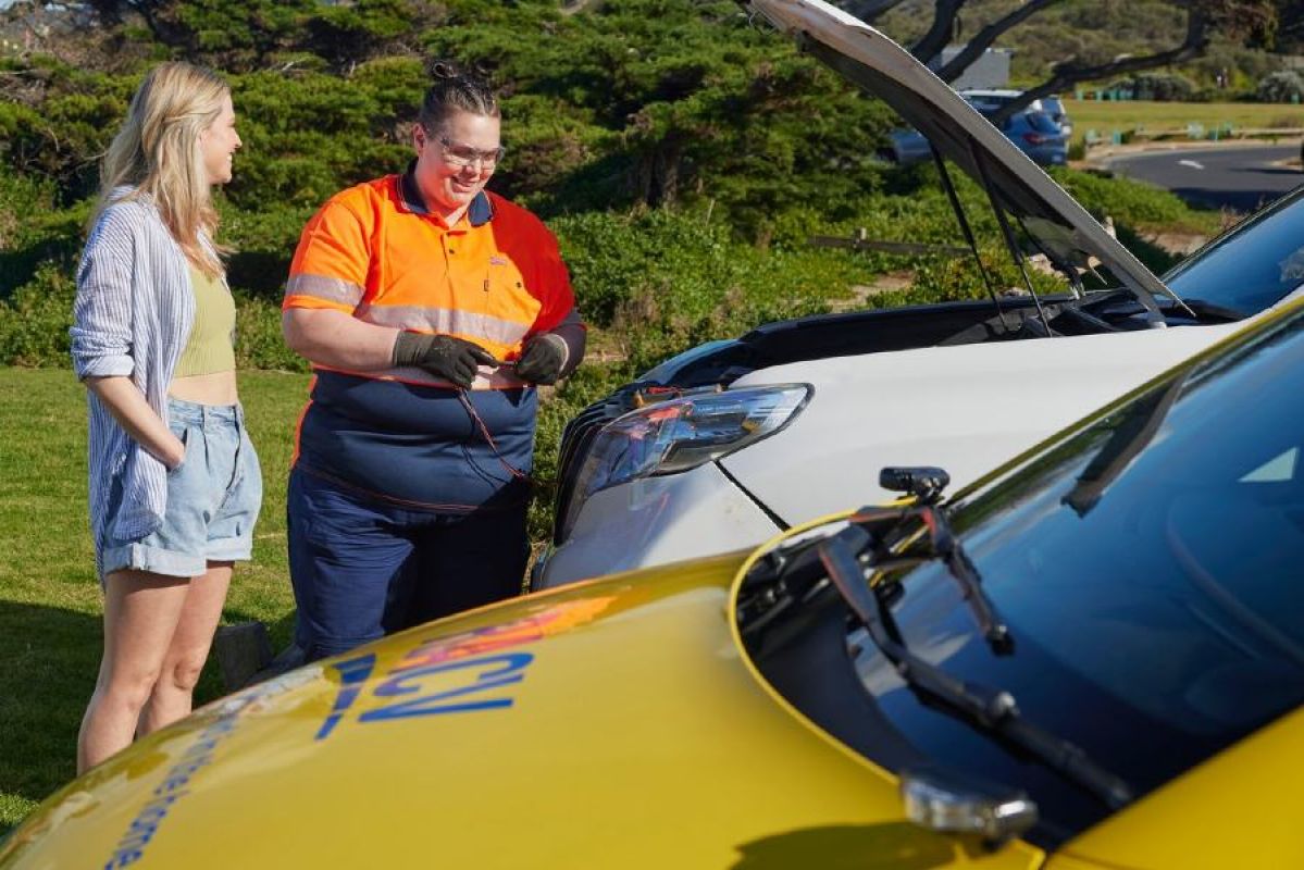 A woman watches on happily as an RACV Emergency Roadside Assistance technician works on their vehicle