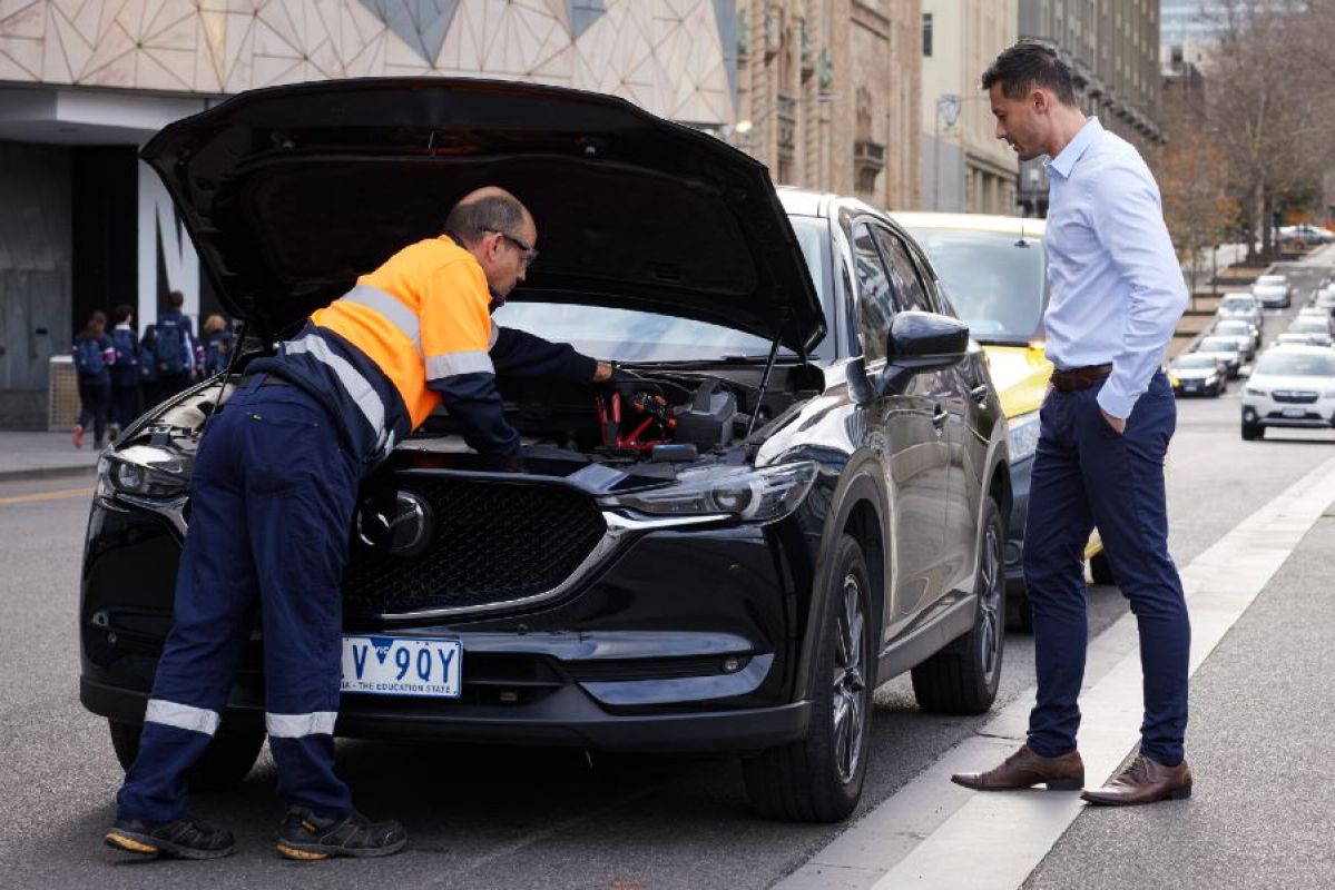 An RACV Emergency Roadside Assistance technician looking under the bonnet of a black SUV parked in the Melbourne CBD