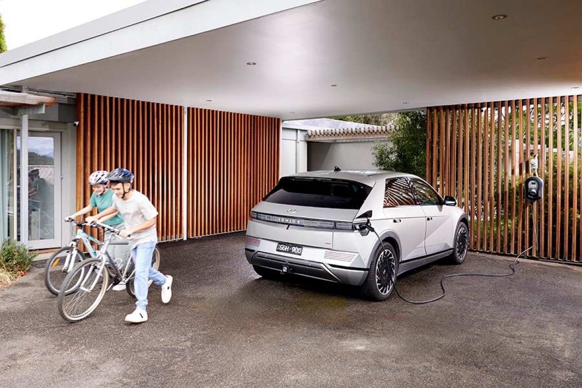 White Hyundai Ioniq 5 EV being charged in carport of suburban house next to two children with bicycles
