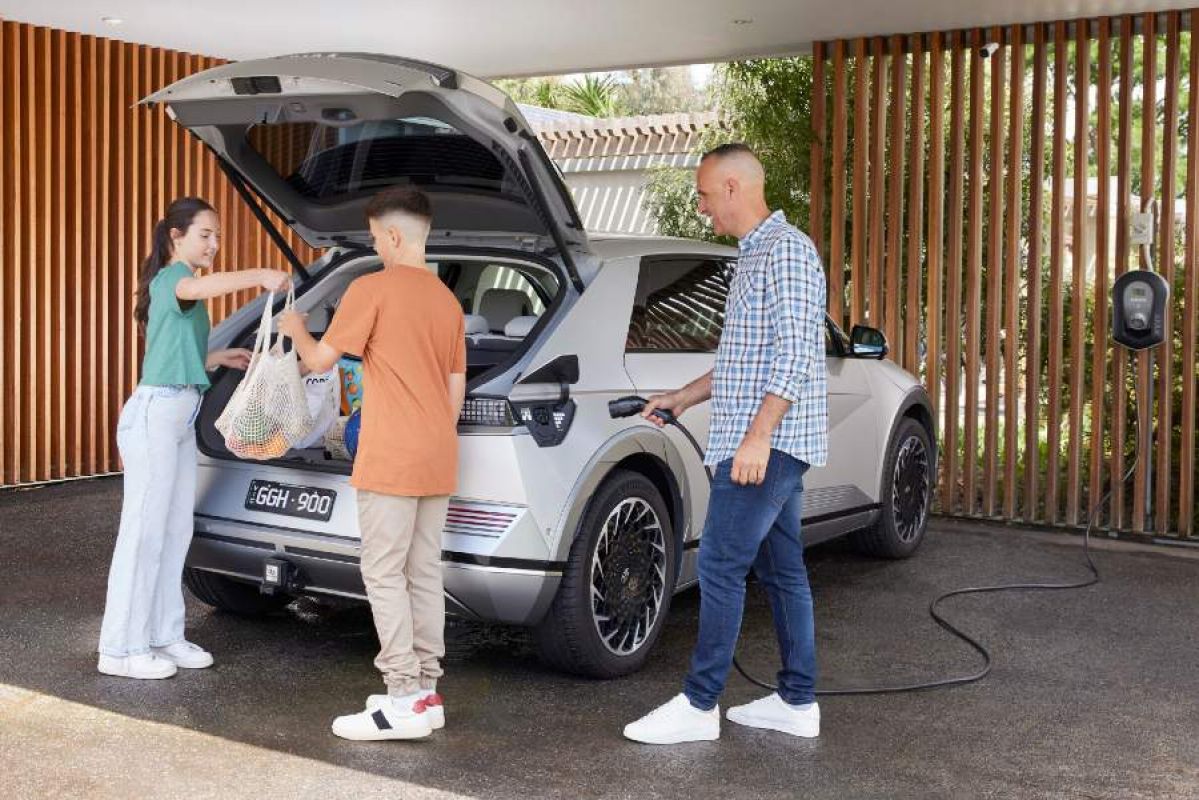 father plugging EV in at home while his children unpack groceries from car