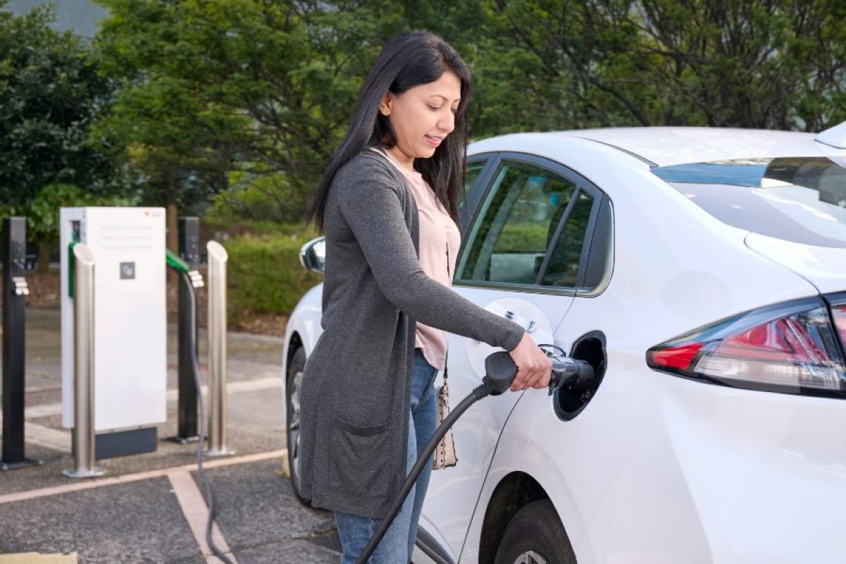 A woman her white EV at a public EV charger
