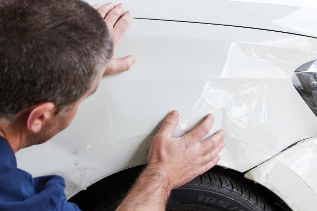 A panel beater assessing the damage on the front  fender of a white car
