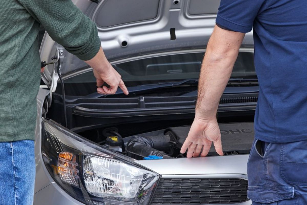 Two people pointing at and inspecting a car's engine under the bonnet