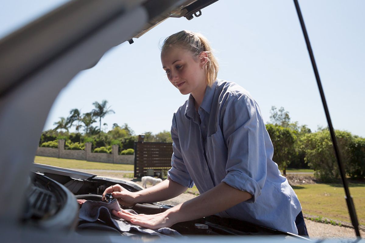 Young woman in grey shirt checking the engine of her car under the bonnet