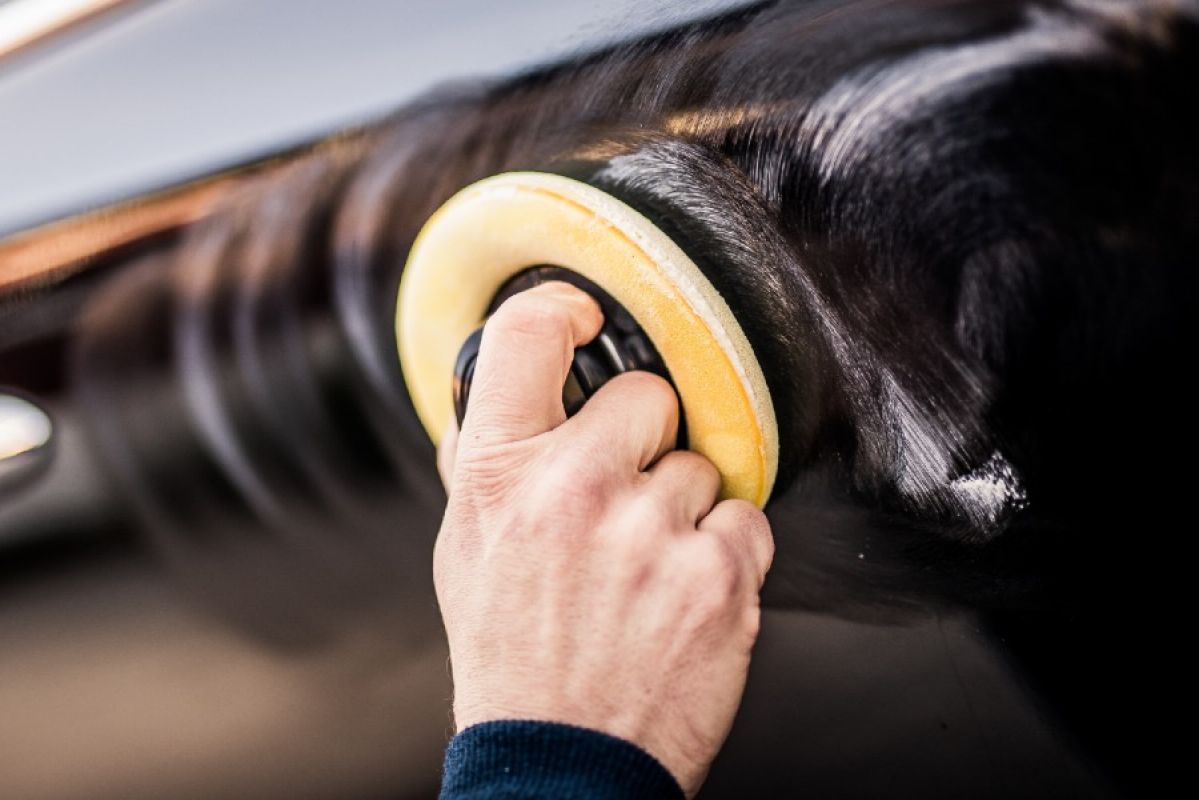 man using a handheld polishing machine on car paint