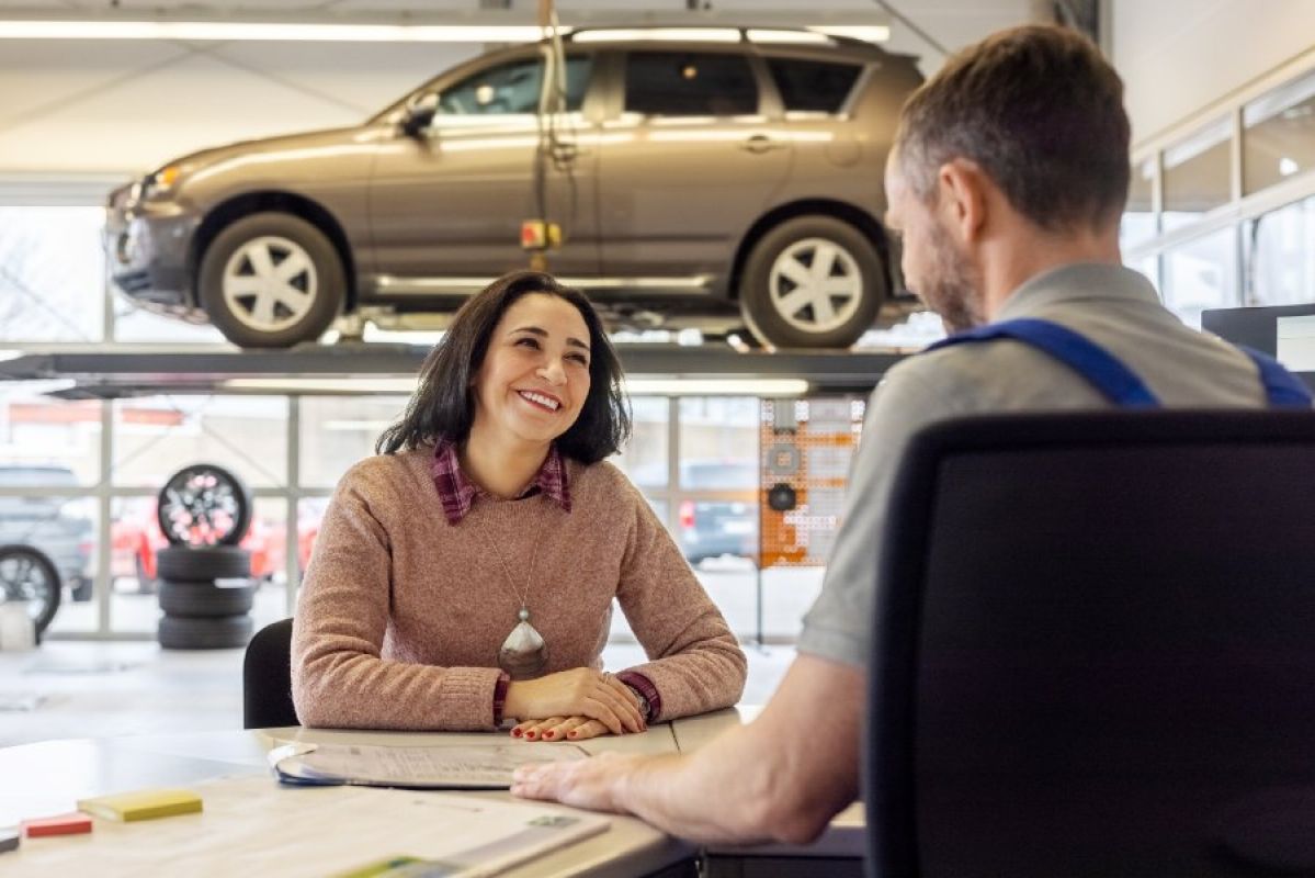 car mechanic speaking to car owner in workshop with elevated car in background