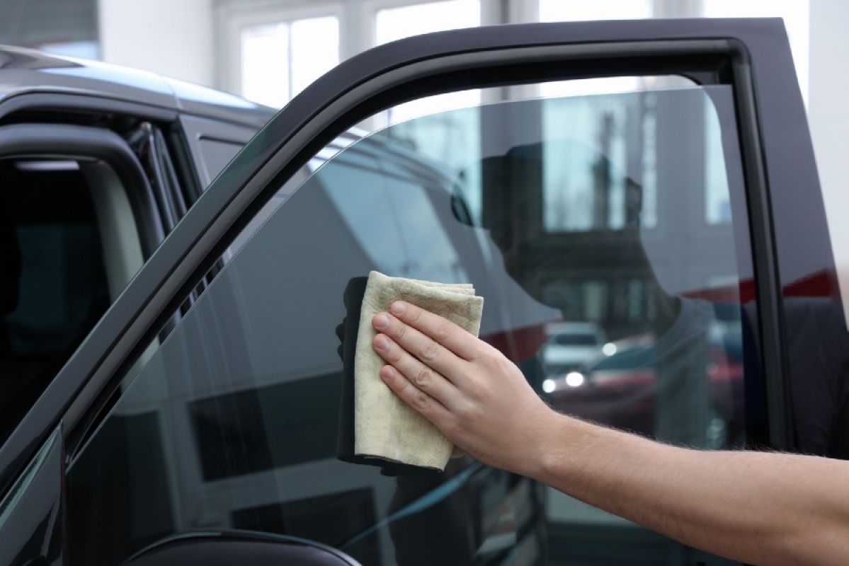person wiping dark tinted car window