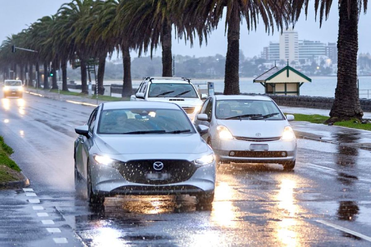 Cars driving along Beach Road in Melbourne on a dark and rainy afternoon.  Each car has its headlights on.