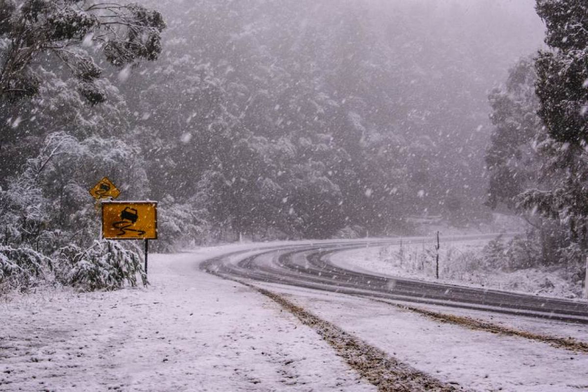 A snowy mountain road in Australia. A yellow road sign warning of slippery roads can be seen on the left.