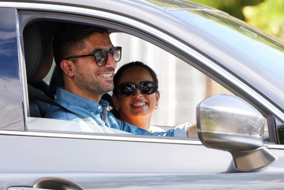 A man and  a woman wearing sunglasses smiling in a  car
