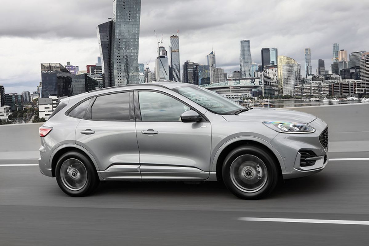 Silver Ford Escape PHEV SUV driving on Bolte Bridge in Melbourne with Docklands and city CBD behind.