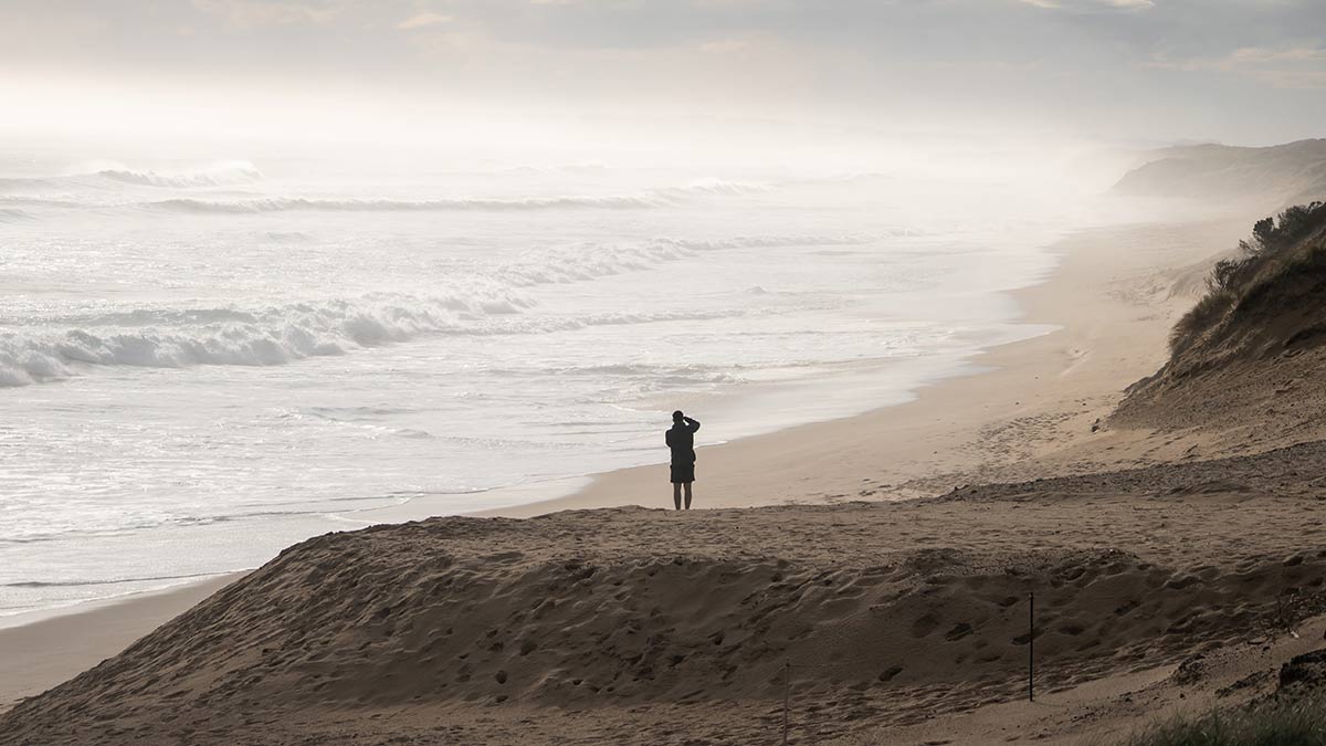 Man standing on dune at Cape Woolamai looking at wild surf