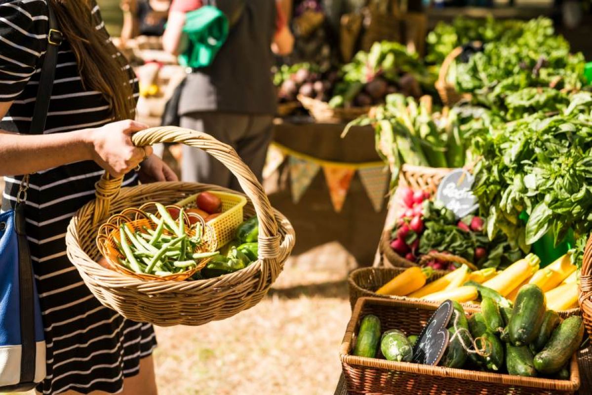 woman holding basket of vegetables at a farmers market