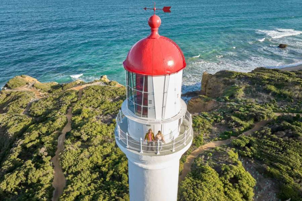 two people standing on observation deck of Split Point Lighthouse with ocean in background