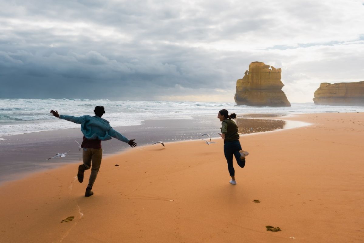 two people running down a beach with the 12 Apostles in background