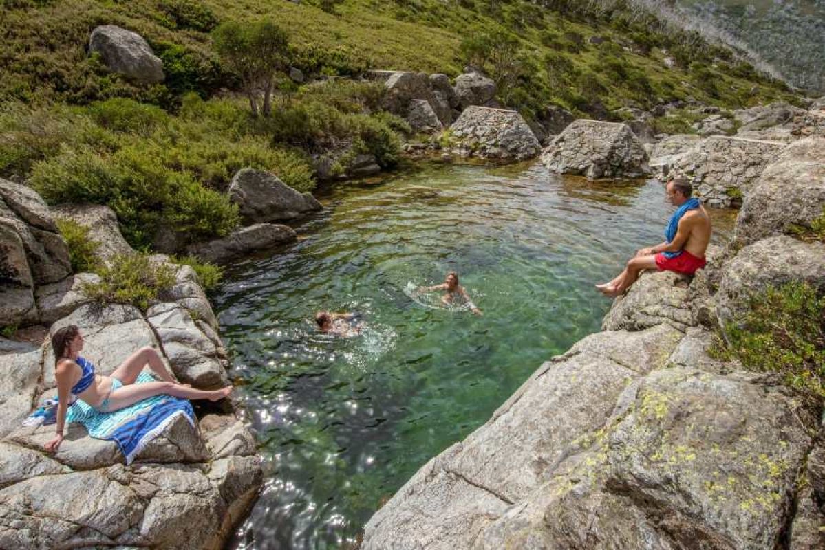people swimming and sunbathing in clear swimming hole